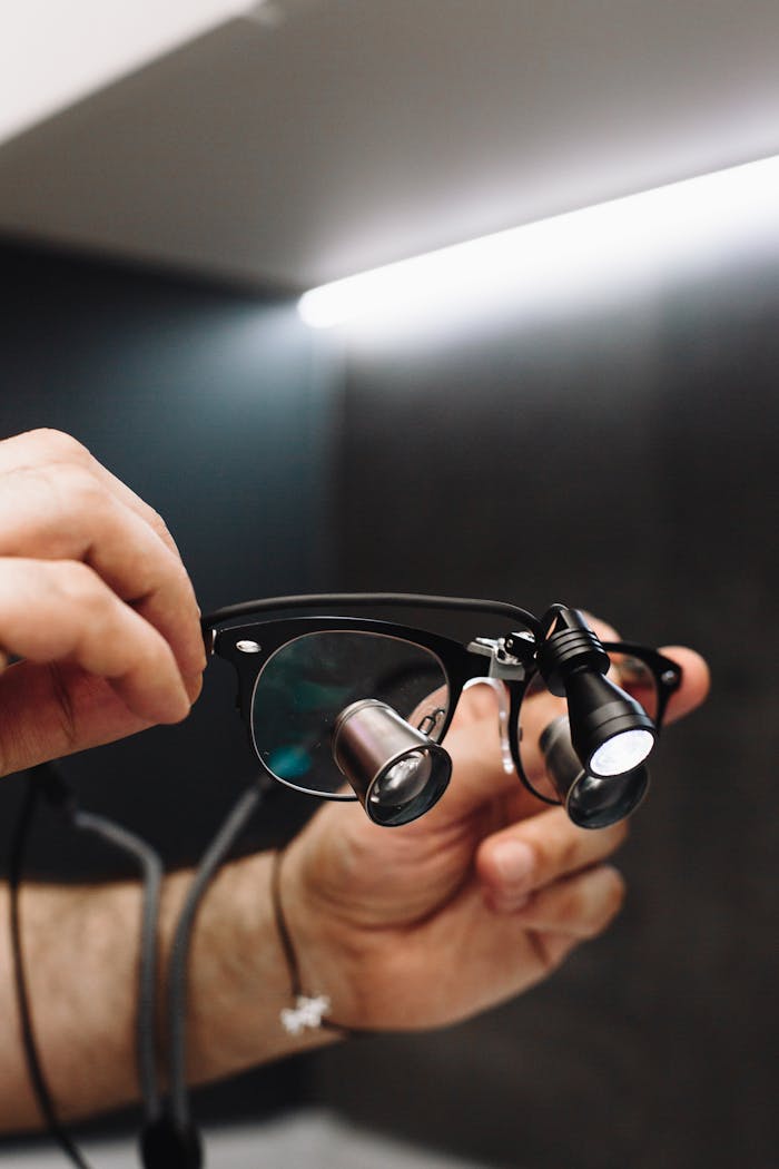 Hands holding dental magnifying loupes, essential for precision in dentistry.